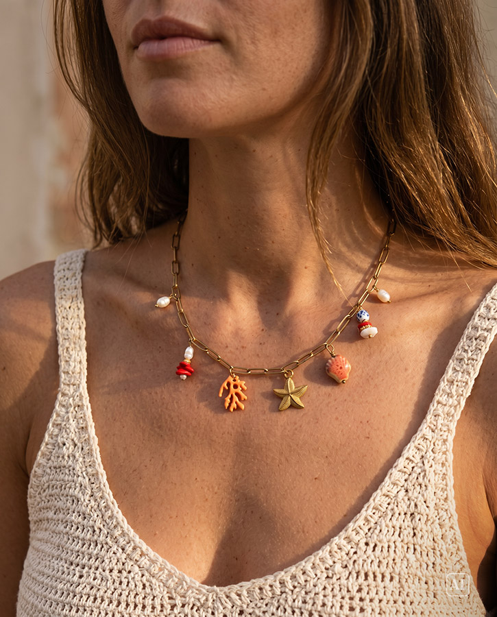 Junge Frau it dunklen Haaren und sommerlicher Kleidung trägt eine Kette mit Charms im Maritimen Look