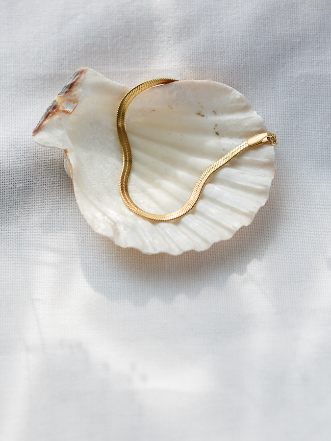 Flaches Schlangenarmband Gold auf hellem Stoff