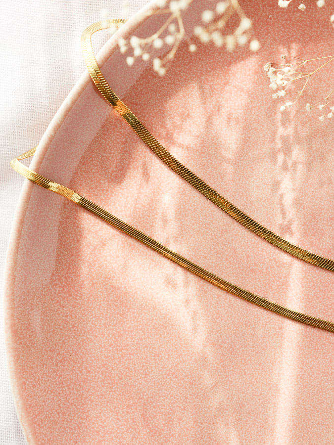 Zwei einzelne flache Schlangenketten CHLOE in Gold auf rosa Keramik