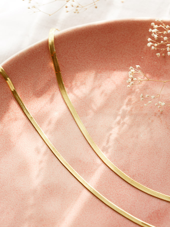 Zwei einzelne flache Schlangenketten CHLOE in Gold auf rosa Keramik